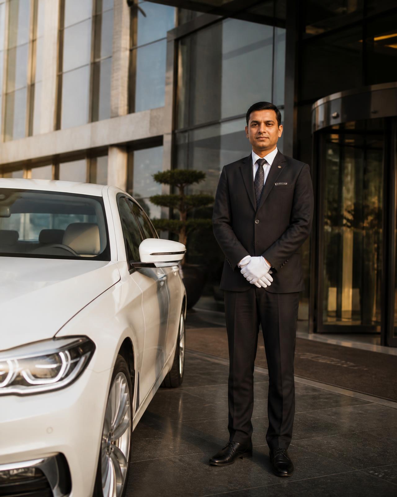Professional chauffeur beside a white executive sedan at a corporate office entrance